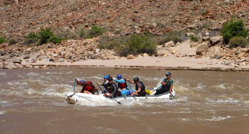 A group of students paddle a raft on choppy water